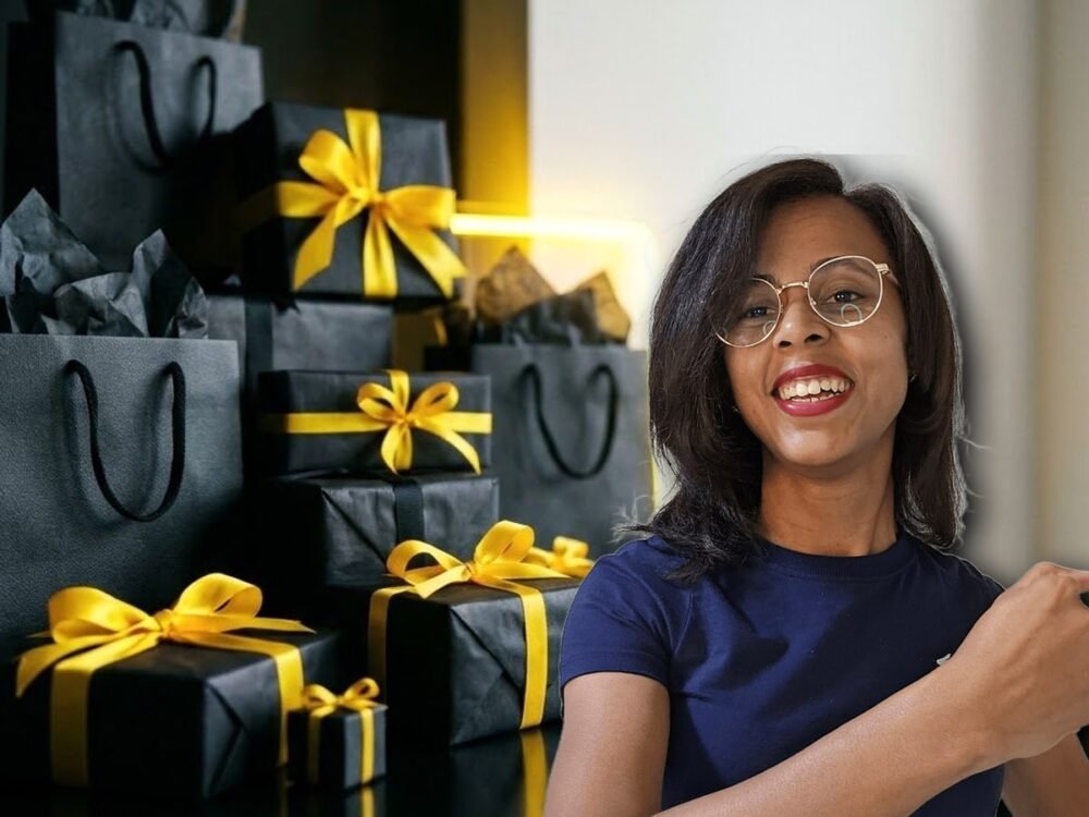 Graciele Fernandes sorrindo ao lado de uma mesa escura com caixas de presente pretas e laços amarelos de Black Friday