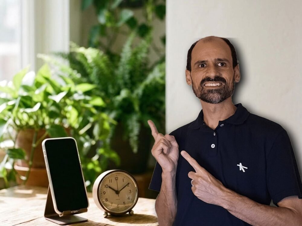 Ailto Rodrigues apontando para o celular apoiado num suporte na mesa de madeira, ao lado de um relógio marcando 10 horas, o horário da sequência de anúncios